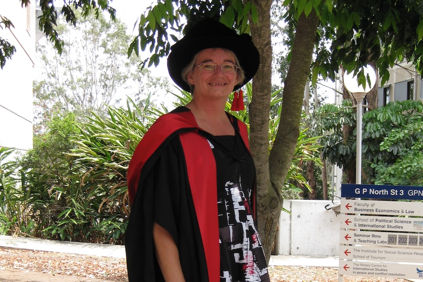 A woman stands in university regalia 