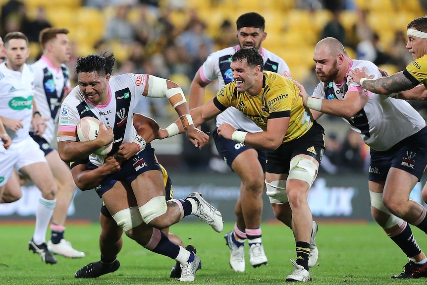 Rugby union player running the ball with opposition players trying to tackle him