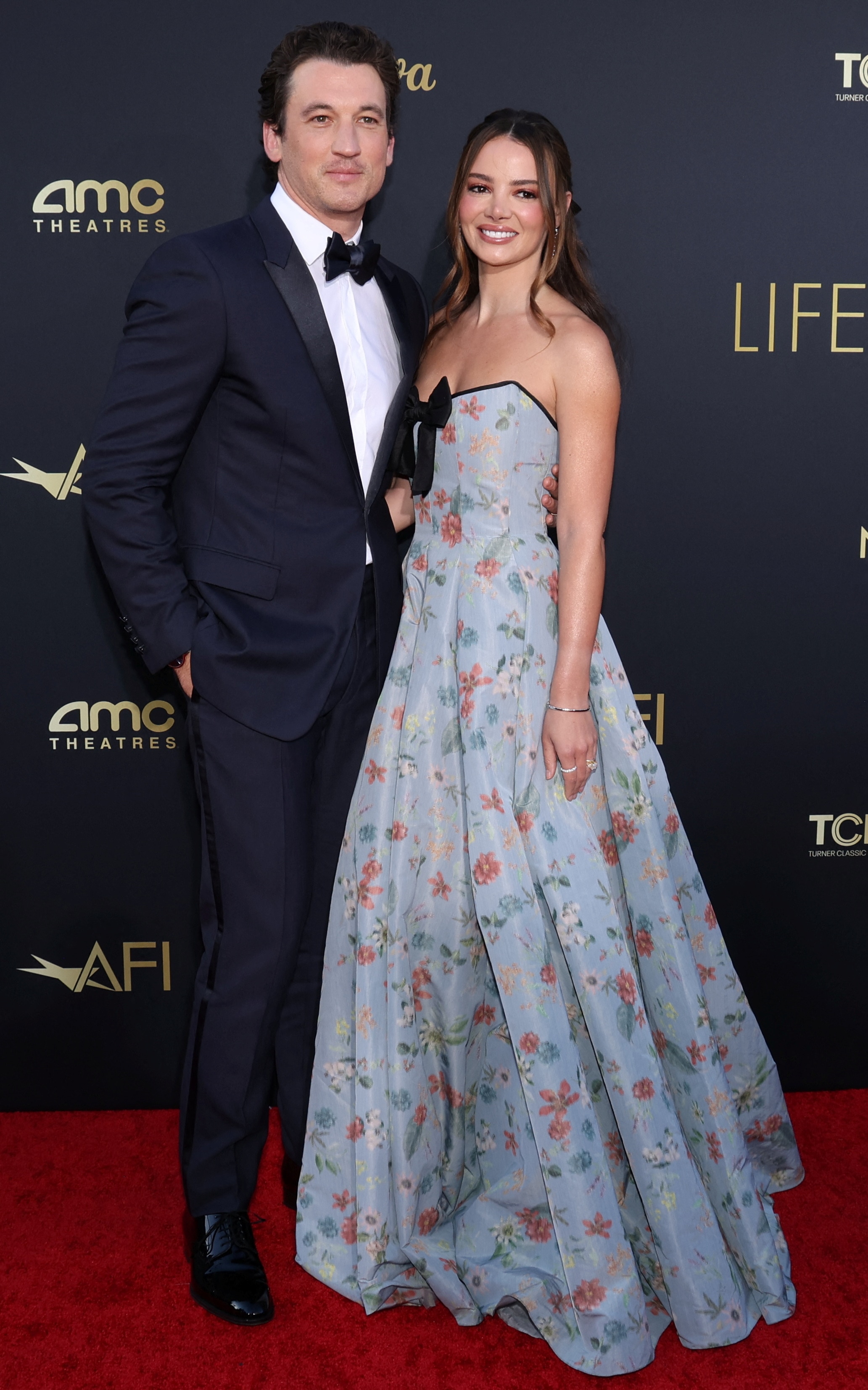 Miles Teller wearing a dark navy suit with a black bow tie and Keleigh Teller in a floral pastel blue strapless gown