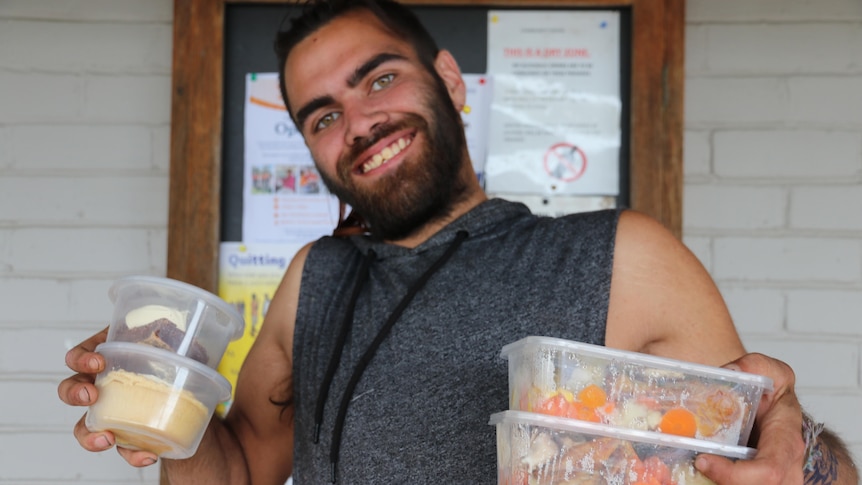 Smiling man holding containers of food up 