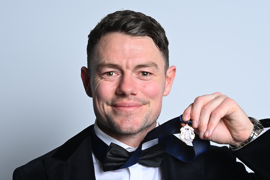 Lachie Neale smiles and holds up the Brownlow Medal