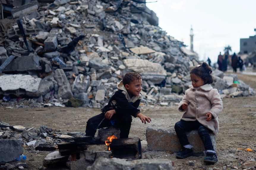 Palestinian children sit by the fire next to the rubble of a house hit in an Israeli strike.
