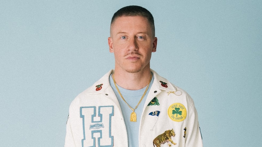 Publicity photo of Macklemore wearing a pressed jacket against grey background