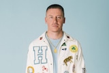 Publicity photo of Macklemore wearing a pressed jacket against grey background