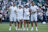 Four tennis players wearing white hold up trophies