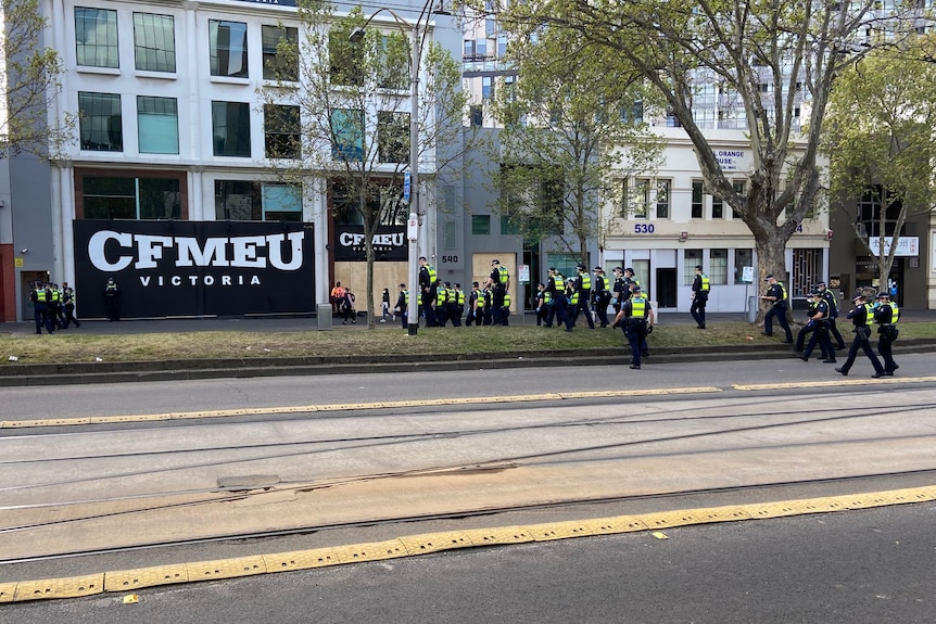 A wide shot of police officers standing on a street next to a CFMEU banner 