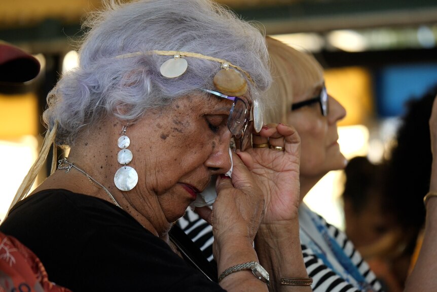 An Indigenous woman uses a tissue to dab her eyes.