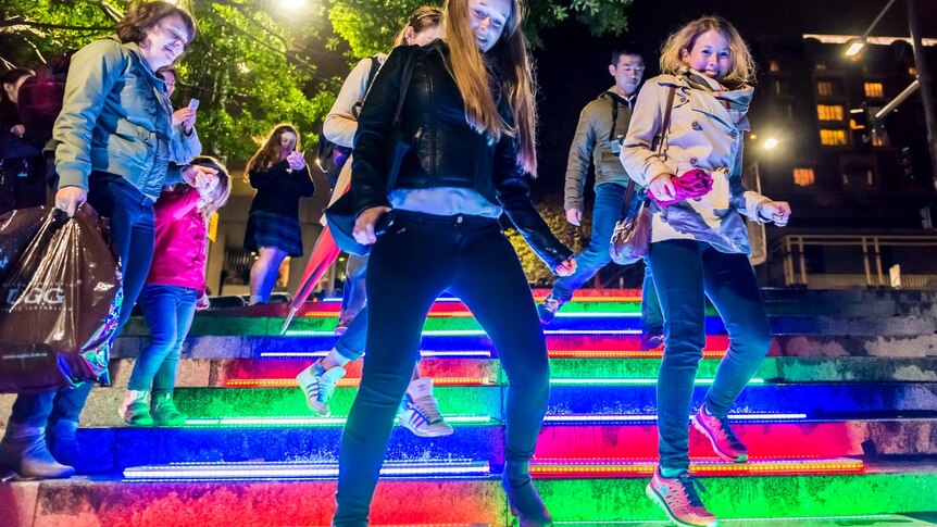 People jumping up and down a set of stairs that light up in multi-colour to the movement.