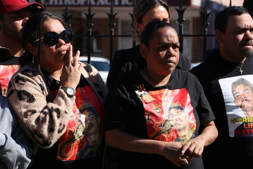 Two women look stern as they wear tee shorts with Gordon Copeland's picture on them.