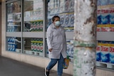 A woman wearing a face mask walks past a shop window filled with washing detergent.