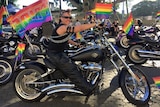 Jules rides on her black Harley with a rainbow pride flag flying on the back.