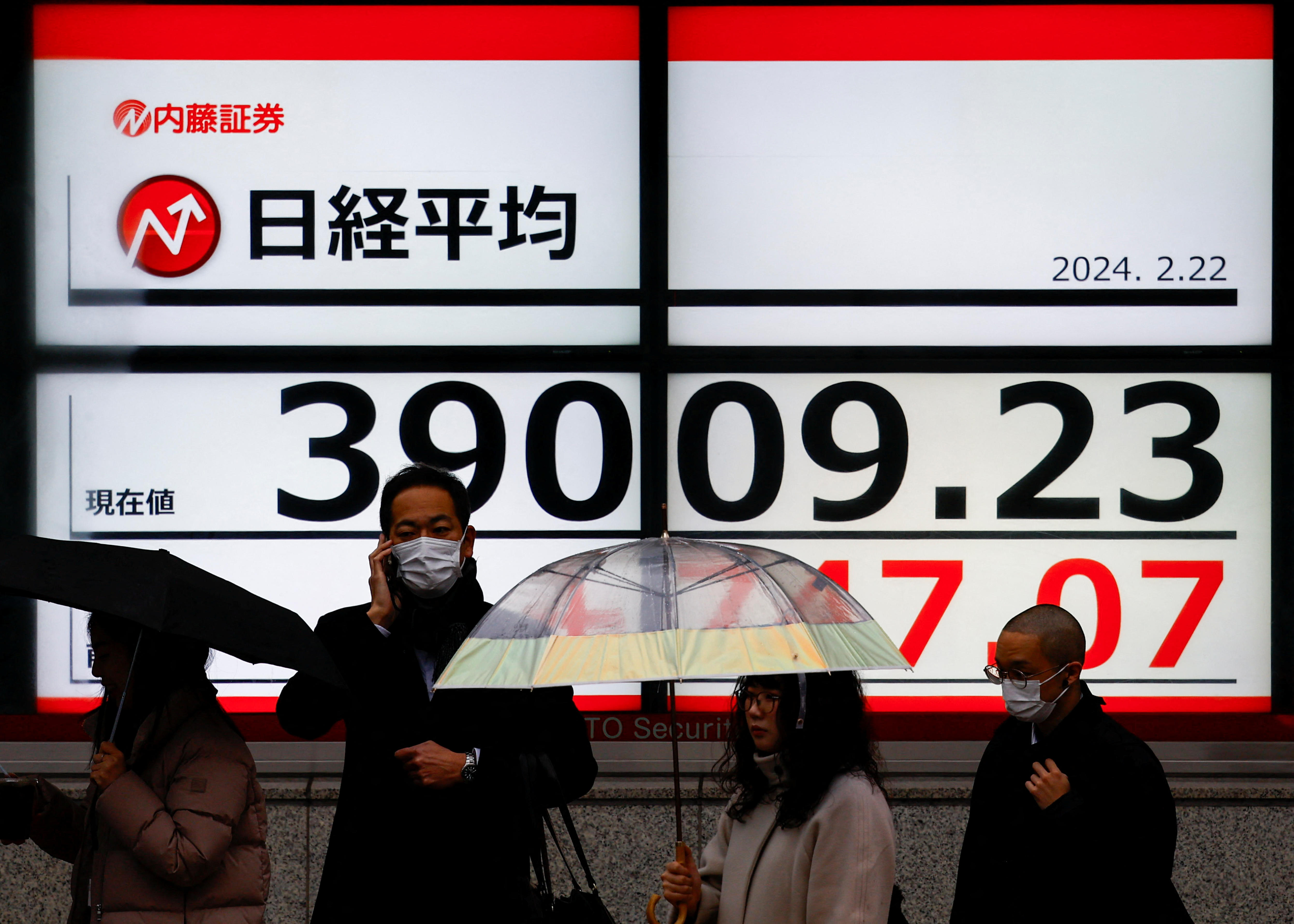 Peopel stand in front of electronic screens displaying Japanese characters and numbers.