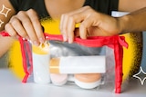 A hand seals up a clear toiletries bag filled with 100ml reusable containers.