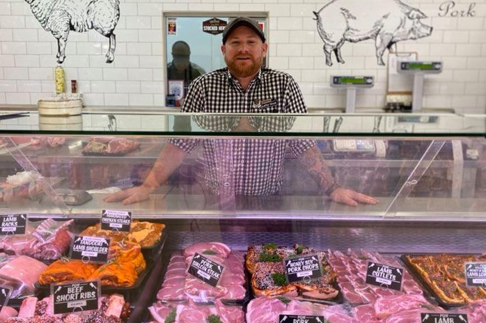 A man in a checked shirt stands behind the counter of a butchery