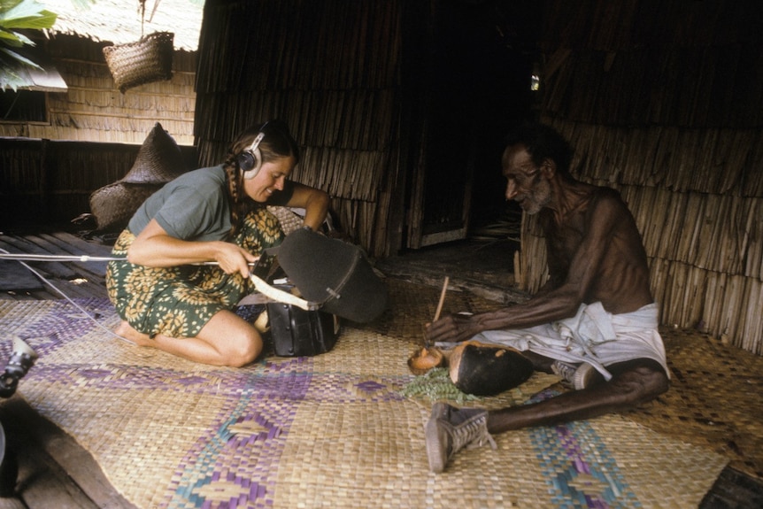 Elizabeth Parer-Cook recording a dugong hunter with a big microphone in a hut in Papua New Guinea