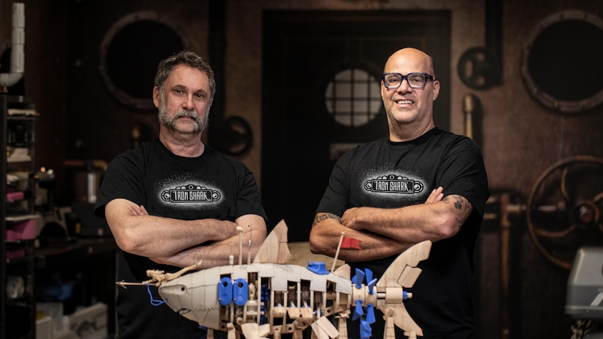 Jon Pryer stands to the left of a wooden model of shark. Chocolatier Dean Gibson stands to the right.