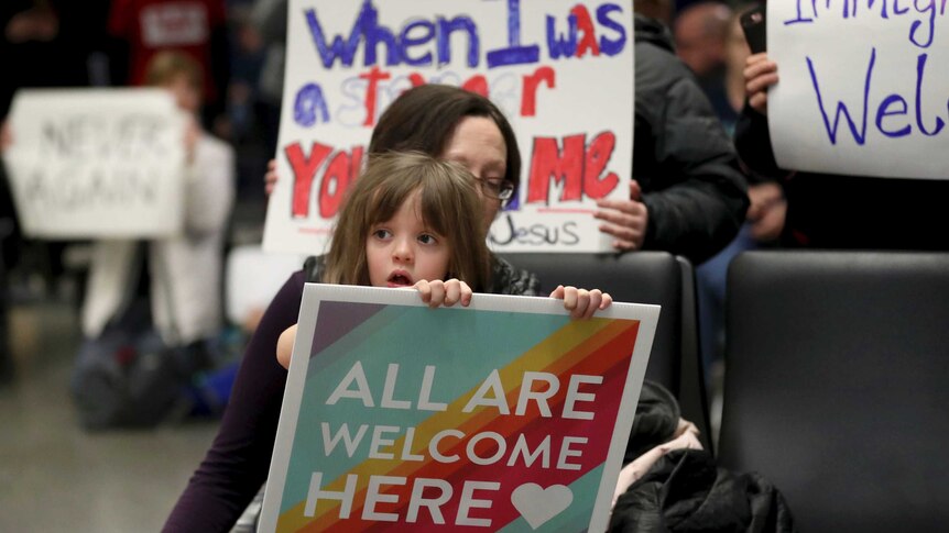 Rachel Walker and her daughter Evelyn, 7, hold signs at Minneapolis-St Paul International Airport