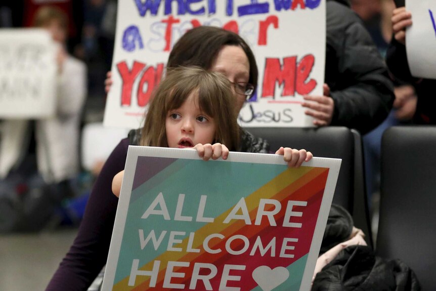 Rachel Walker and her daughter Evelyn, 7, hold signs at Minneapolis-St Paul International Airport