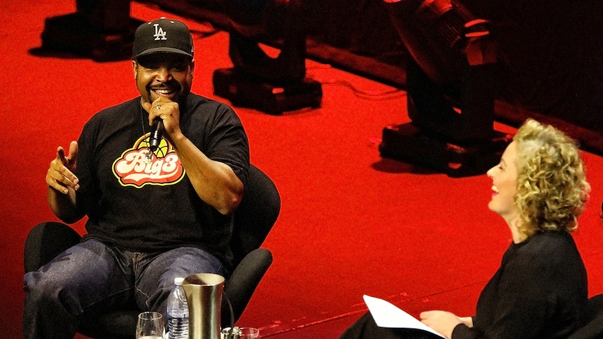 Ice Cube speaks into a microphone and Zan Rowe laughs on stage at the Sydney Opera House