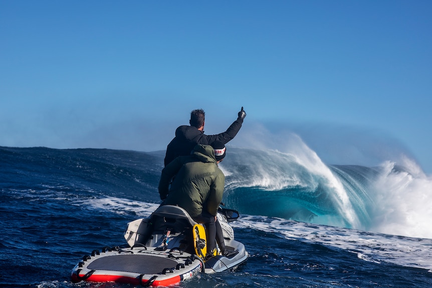 Two young men aboard a jetski eye a huge breaking wave.