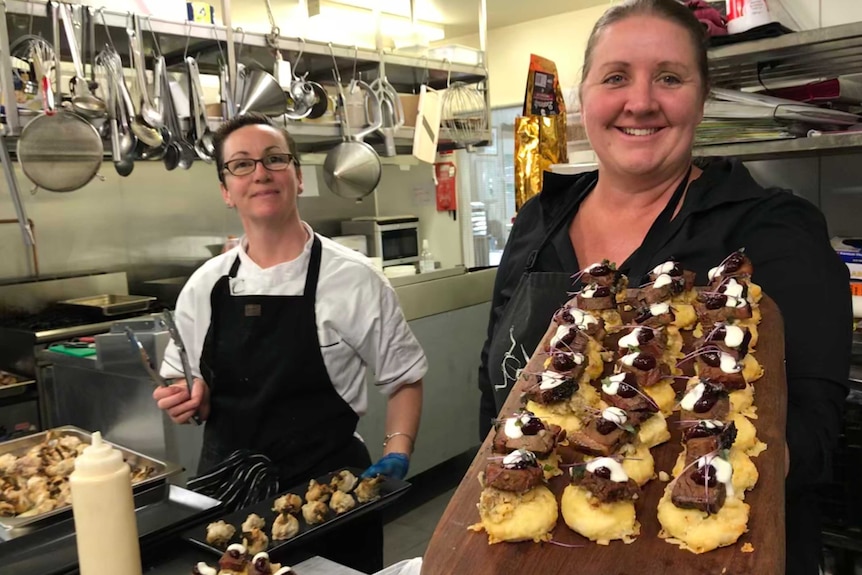 Two people in a kitchen holding out food