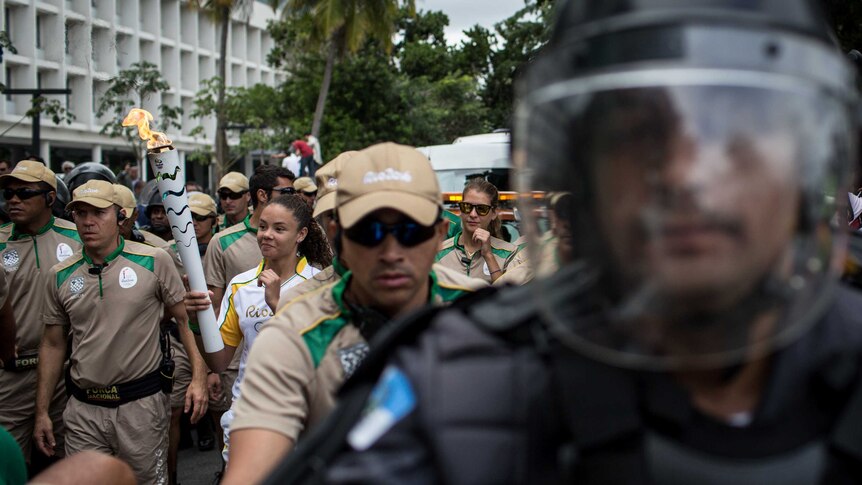 Security guards march alongside Olympic torch in Rio