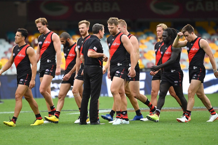 A team of AFL players and their coach walk off the field.