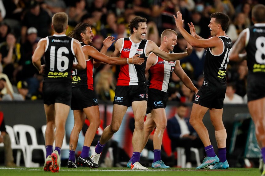 A bunch of St Kilda players gather around a smiling Max King to congratulate him