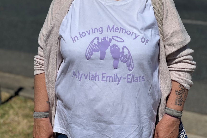 A woman, face unseen, wears a shirt dedicated to the memory of a baby that died.