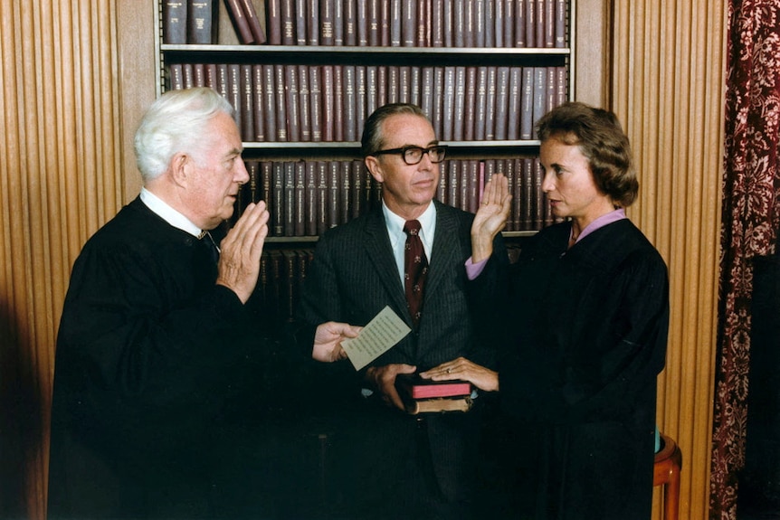 One man with his hand raised standing across from Sandra Day O'Connor with her hand raised and another placed on a bible. 