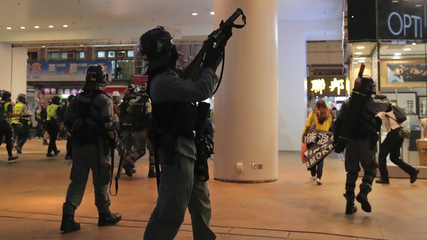 Police wearing riot gear point guns in a shopping centre at protesters