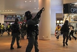 Police wearing riot gear point guns in a shopping centre at protesters