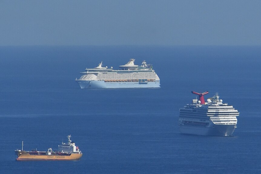 Two cruise ships sailing on blue waters and another ship nearby