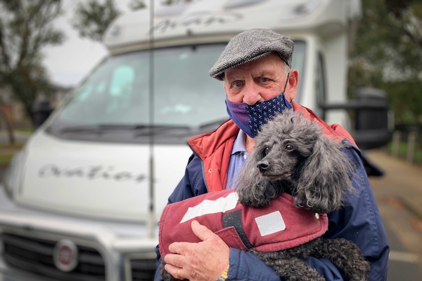 A man with a COVID-19 mask holds a dog.