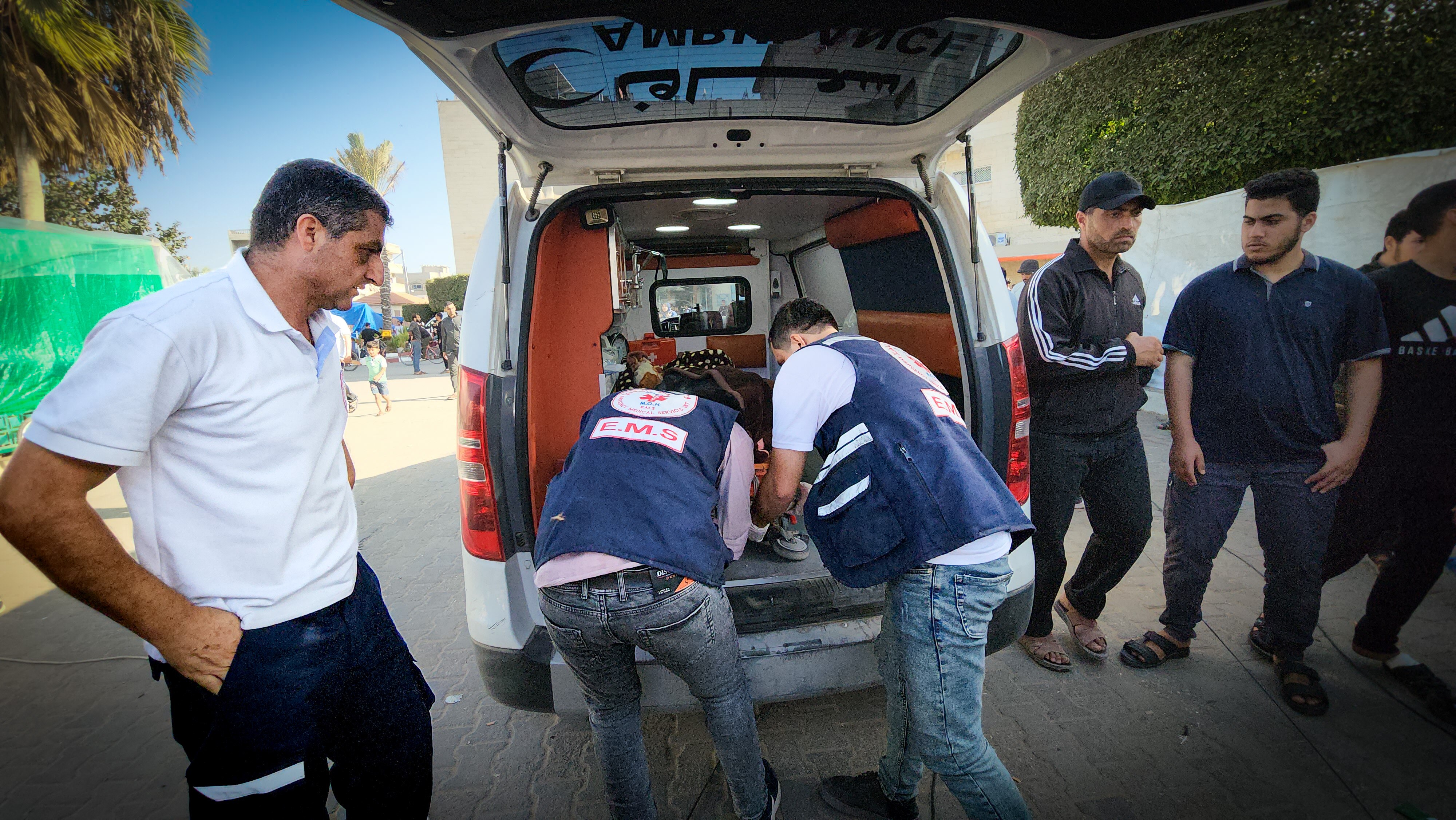 A paramedic watches two men in blue vests looking into the back of an ambulance