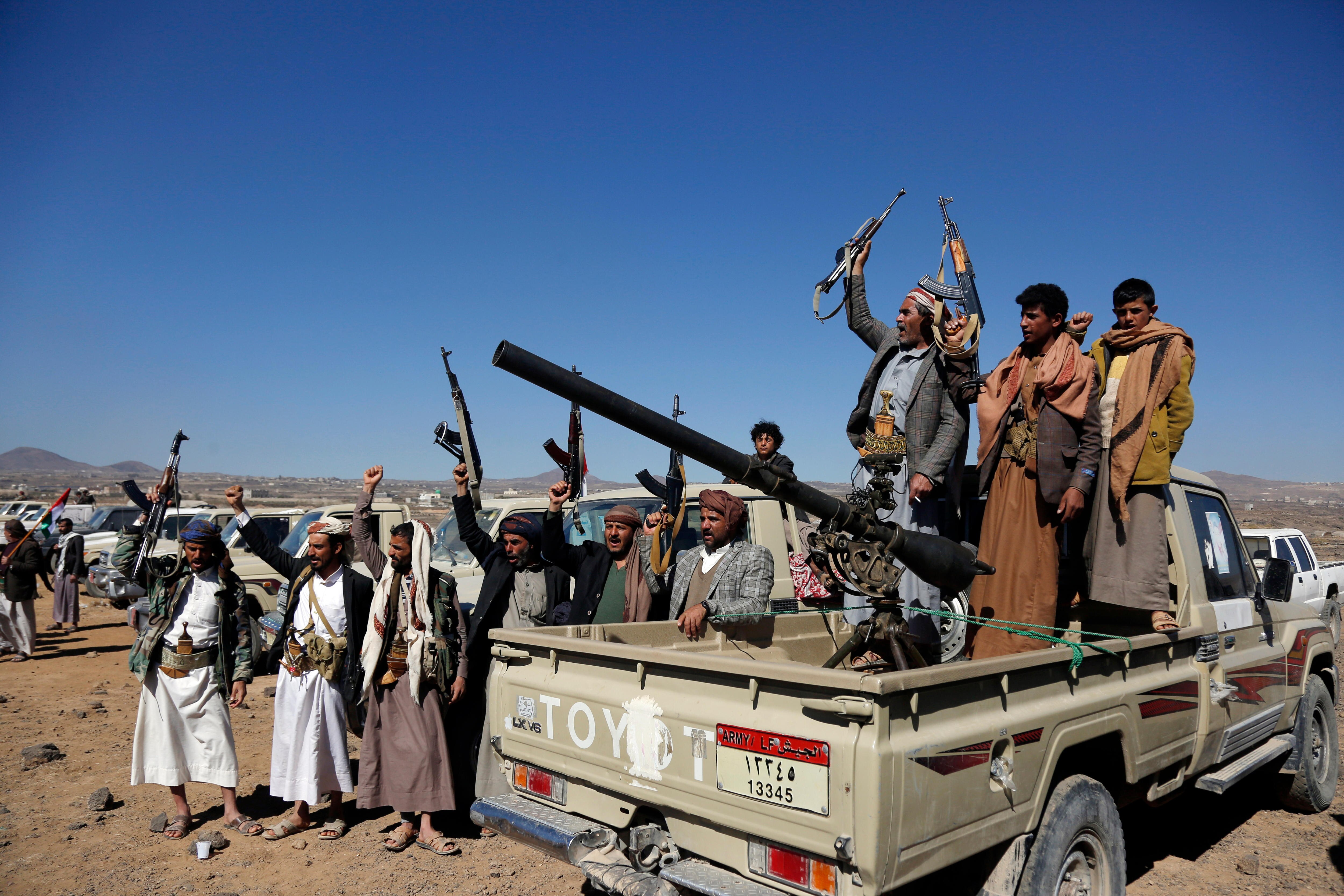 Houthi fighters and tribesmen stand on and around a ute holding up guns.