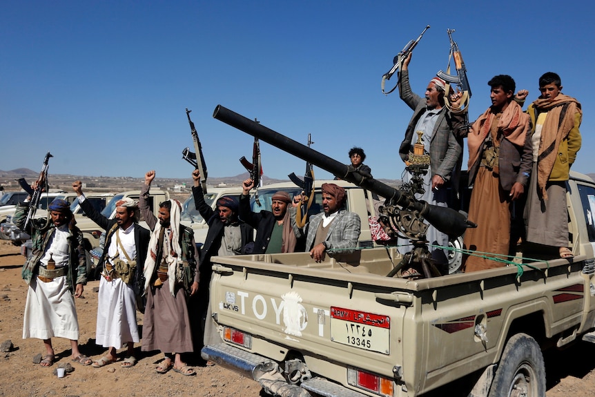 Houthi fighters and tribesmen stand on and around a ute holding up guns.