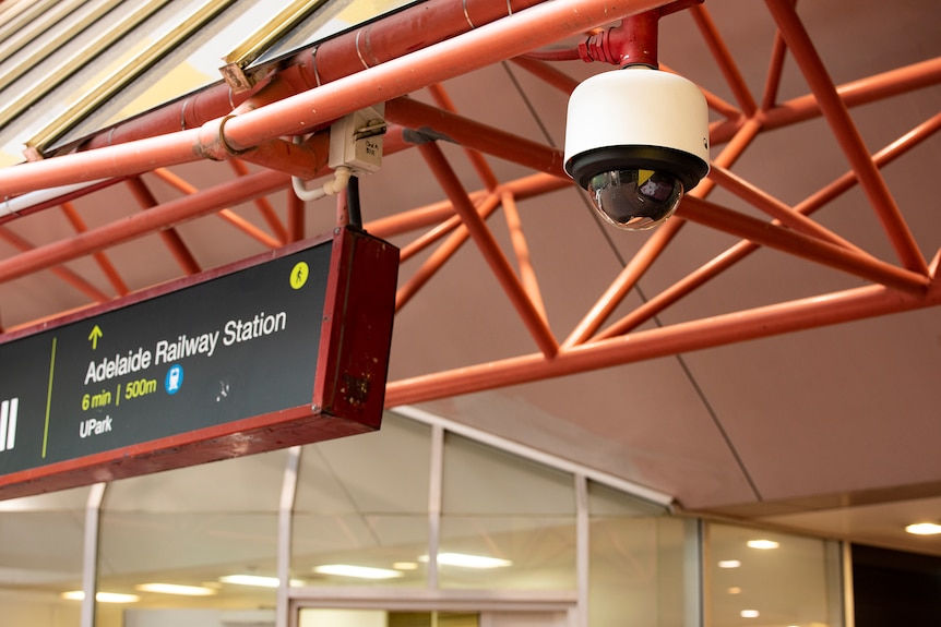 A CCTV camera hangs from the roof next to a sign pointing to Adelaide Railway Station