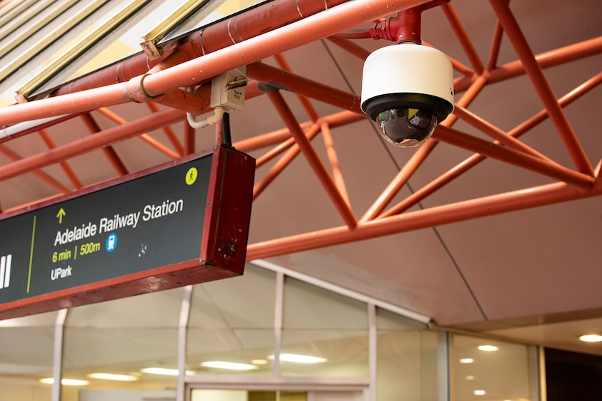 Une caméra de vidéosurveillance est suspendue au toit à côté d'un panneau indiquant la gare d'Adélaïde