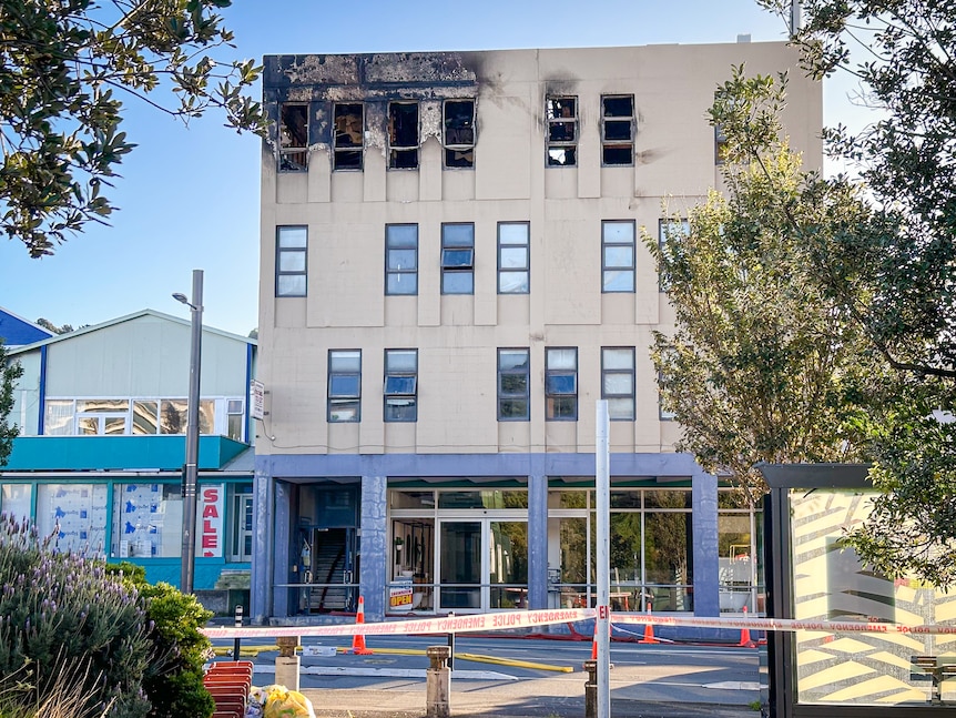 Safety tape is seen cordoning off a four-storey building with visible fire damage to the top floor 