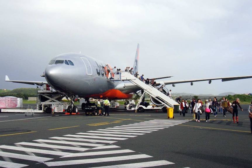 People exit a plane and walk across the tarmac to the terminal.