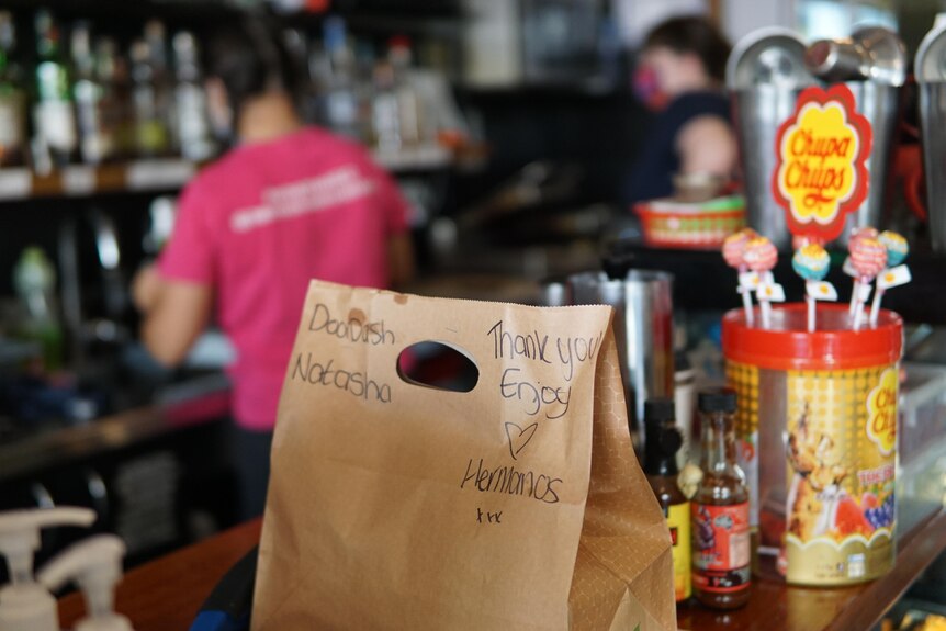 A delivery bag sits on the bar as a staff member prepares something in the background.
