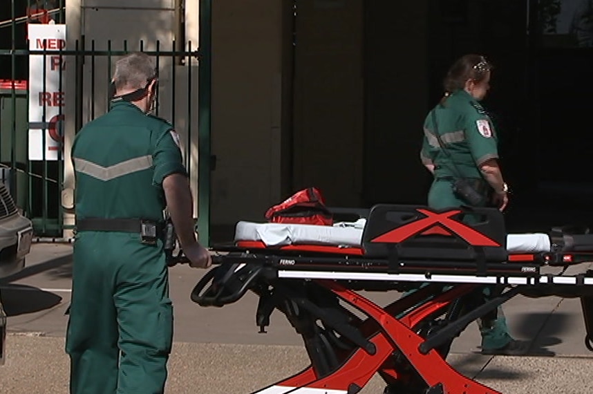 Two paramedics with a stretcher, walking towards a building.