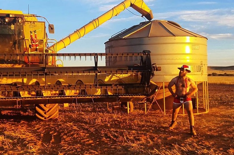 A man poses in his underwear near a harvester in a field