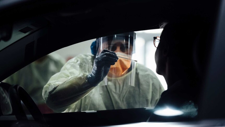 A nurse in personal protective equipment leans into a car to swab a patient at a drive-thru coronavirus clinic.