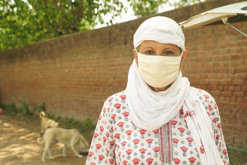 Sonya Gosh in a face mask standing near a brick wall with dogs nearby