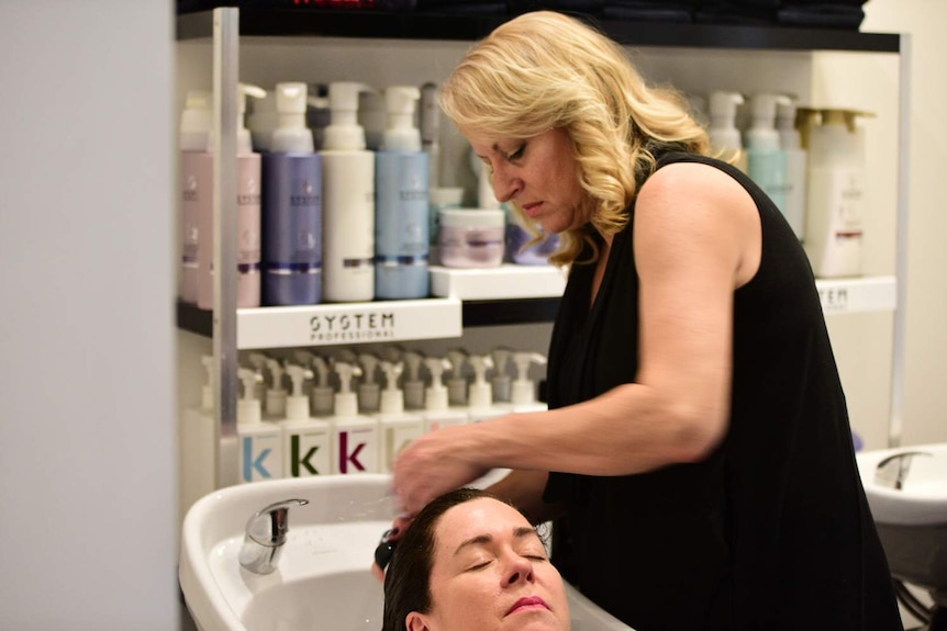 Apprentice Veronica Ford washes a woman's hair in her workplace, a hair salon in Brisbane.