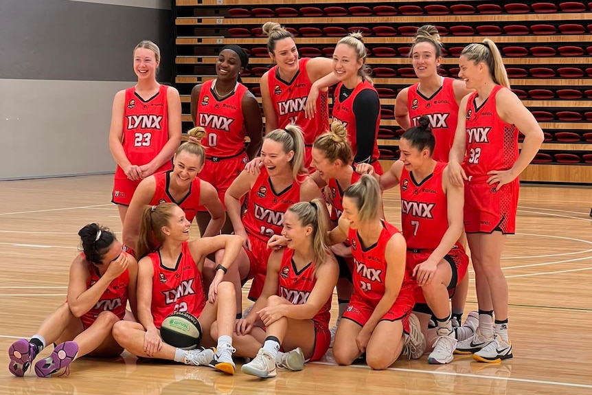 A group of Perth Lynx WNBL players pose for a photo on a basketball court.