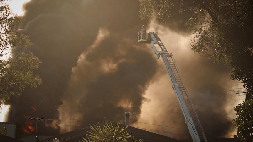 A firefighter on a crane in front a massive plume of smoke.