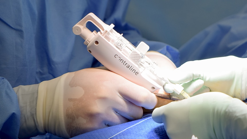 The professor is in surgical scrubs and holds an implant machine